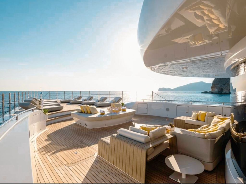The 208 Benetti II yacht sailing away from a tropical island with lush green hills and clear blue water.
