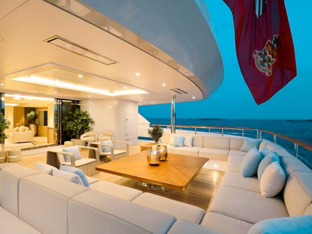A large luxury yacht, 208 Benetti II, anchored near a tropical island with green hills and calm, clear waters.