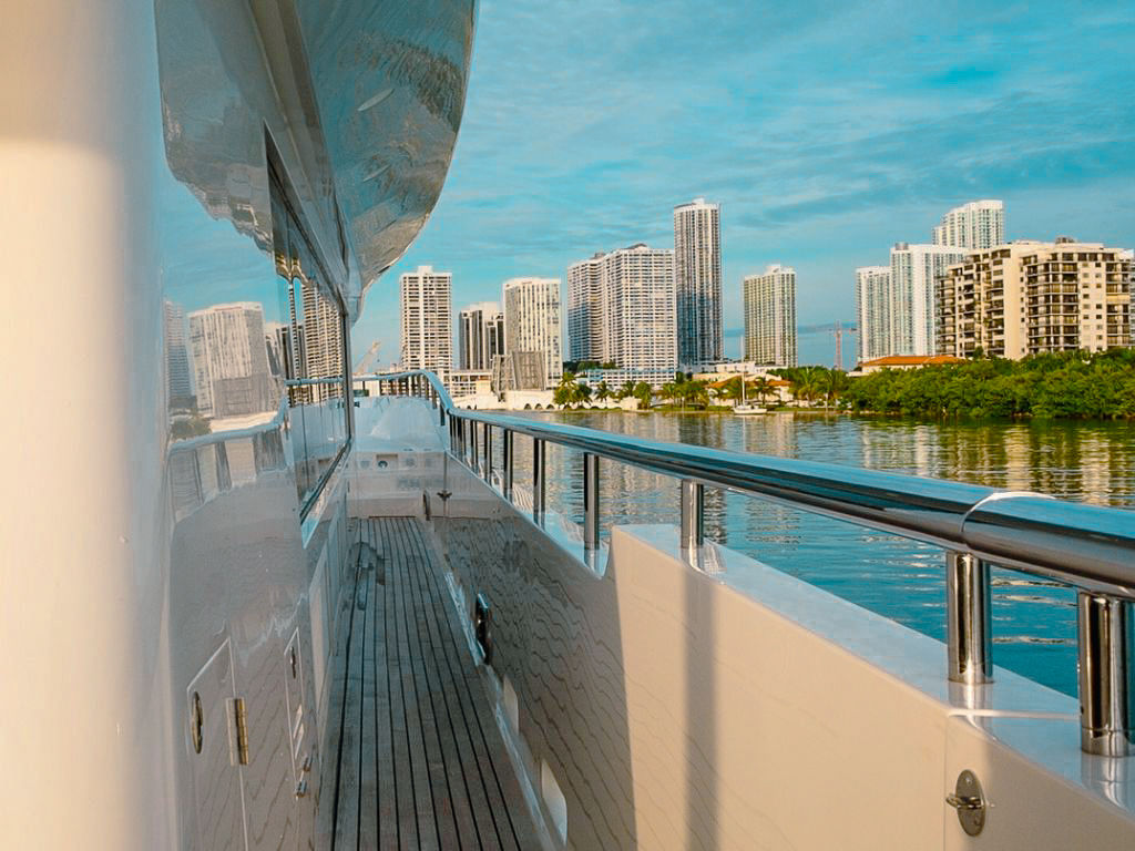 Guests relaxing on the front deck netting of the 103 Johnson  yacht with Miami in the background